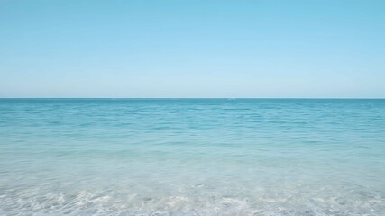 Obraz premium Serene ocean under clear blue sky, calm waves reflecting sunlight, peaceful atmosphere