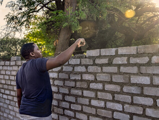 african bricklayer with a trowel ,building a surrounding bricks wall, late afternoon