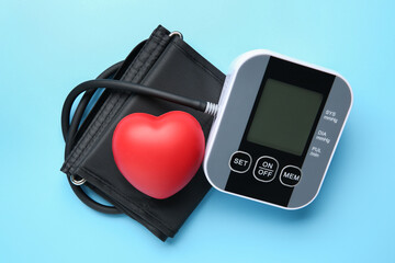Blood pressure measuring device and squeeze heart on light blue background, top view