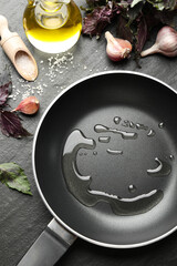Frying pan with cooking oil and products on dark textured table, flat lay