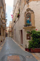 A narrow street with a statue of Mary and a few potted plants