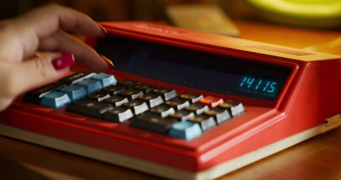 Close-up of the retro calculator screen. A woman's hand enters the numbers