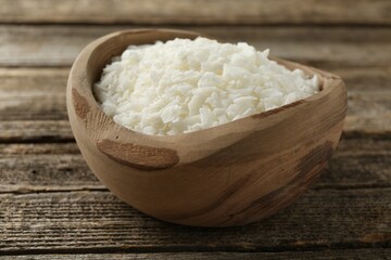 White soy wax flakes in bowl on wooden table, closeup