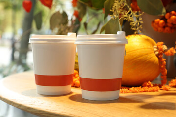Paper cups with hot drinks and autumn decoration on wooden table in cafe
