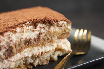 Piece of tasty tiramisu and fork on black table, closeup