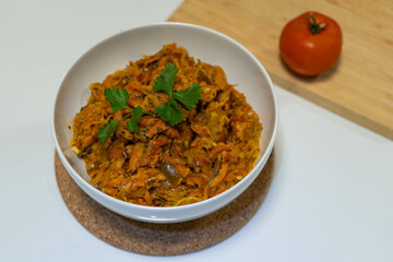A dish of stewed vegetables, including zucchini, on a white table, garnished with parsley, focusing on healthy eating.