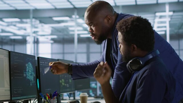 Data center manager helps intern implement AI predictive maintenance systems. Server farm supervisor checks work done by employee using artificial intelligence to identify hardware failures, camera A