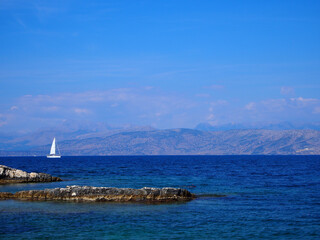 A single white sailboat in front of hills in the ionian sea in Corfu, Greece