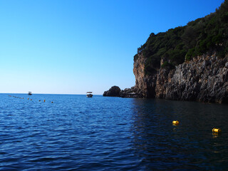 Boats anchored next to the cliffside mountains on the coastline of Corfu, Greece