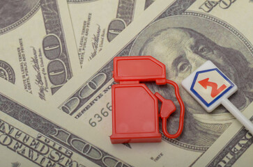 A toy gas pump and a sign symbolizing rising fuel prices rest atop a bed of US dollar bills,...
