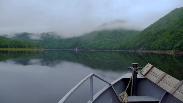 Zeya Reservoir. A boat sails along the calm waters of the lake among green coniferous hills.