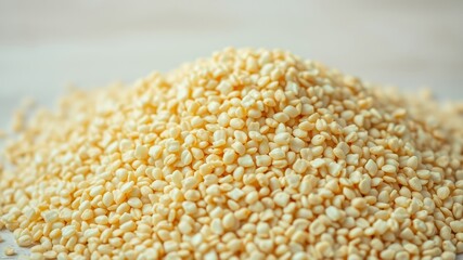 A close-up view of a heap of uncooked, light yellow grain-like pasta pieces on a wooden surface