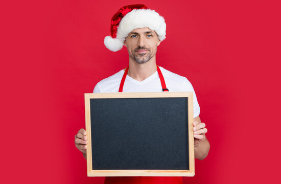 positive mature man in christmas hat and apron hold blackboard with copy space