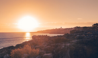 The setting sun casts a warm golden glow over the rugged coastline of cascais, portugal, creating a breathtaking scene of natural beauty and tranquility