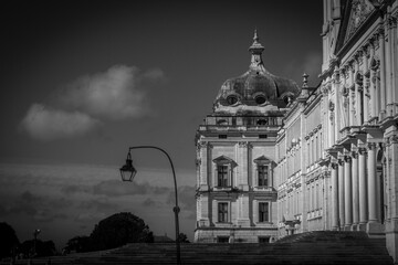 Dramatic black and white photo of the royal palace of mafra in portugal, with a vintage lamppost in front and intricate facade reaching towards the sky