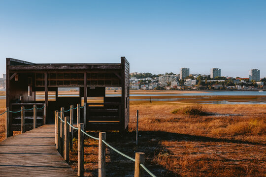 Wooden bird hide with walkway and rope railing offering scenic views of urban skyline across douro river estuary in vila nova de gaia, porto, portugal. Estu&aacute;rio do Douro Local Nature Reserve