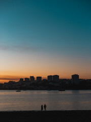Two people are enjoying a beautiful sunset over the douro river with the cityscape of Porto in the background, creating a serene and romantic atmosphere. From Cabedelo, Vila Nova de Gaia, portugal