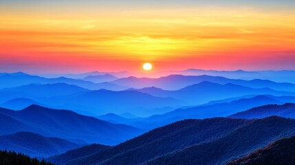 A vibrant sunrise paints the sky with hues of orange, pink, and yellow as it peeks over a vast expanse of layered blue mountains.