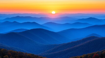 Fototapeta premium A vibrant sunset over a range of blue mountains, with a hazy golden sky above.