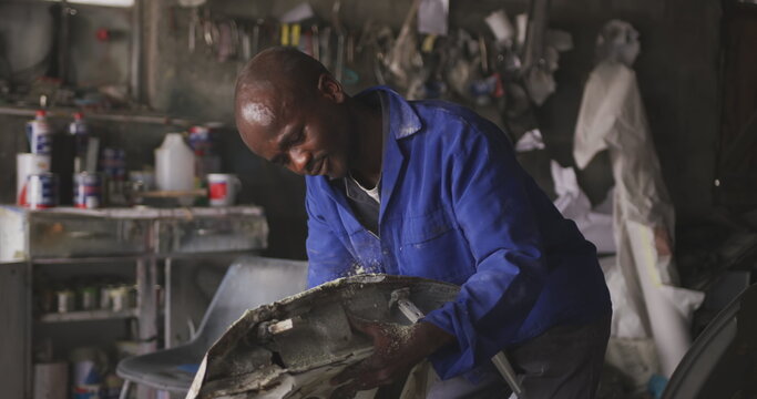 Front view of an African male panel beater in a township workshop, sanding and preparing surface of - Powered by Adobe