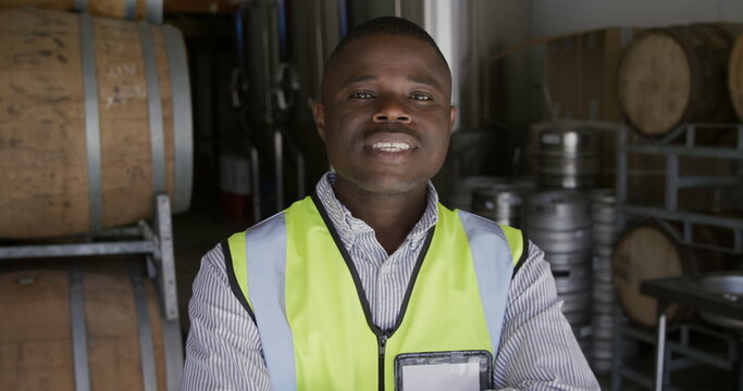 Portrait of an African American man working in a microbrewery, wearing high visibility vest and look - Powered by Adobe