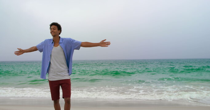 Rear view of African american man standing with arms outstretched on the beach