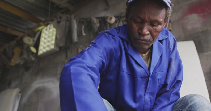Front view of a senior African male panel beater in a township workshop, cleaning an alloy whee