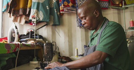 Side view of an African male tailor in a township workshop, using a sewing machine