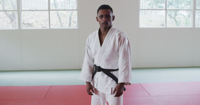 Front view of a teenage Biracial male judoka wearing white judogi, warming up before a training in a
