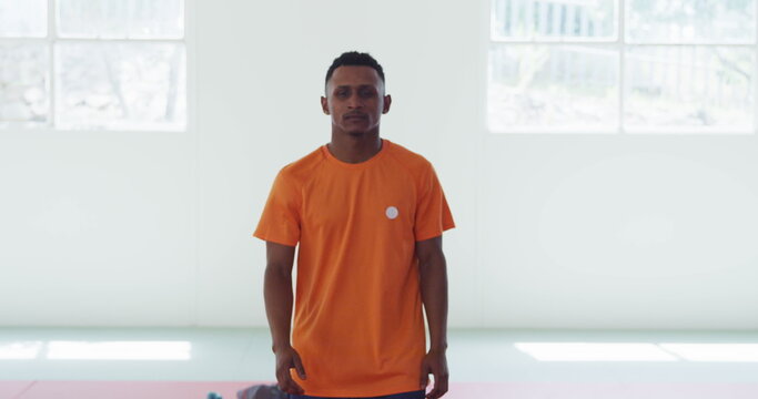Portrait of a happy biracial teenage male judoka wearing orange t-shirt, standing with arms crossed
