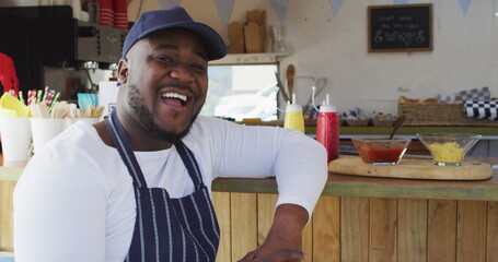 Portrait of african american man wearing apron smiling while standing near the food truck
