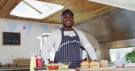 Portrait of african american man wearing apron smiling while preparing burgers in the food truck