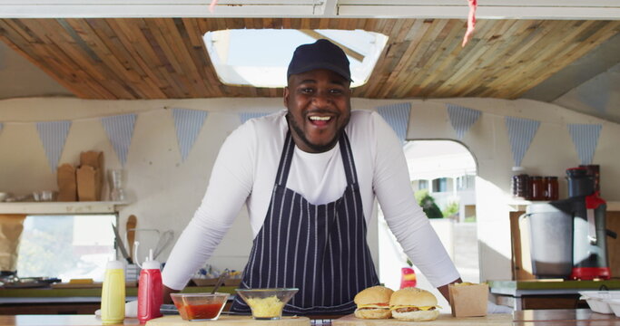 Portrait of african american man wearing apron smiling while standing in the food truck - Powered by Adobe