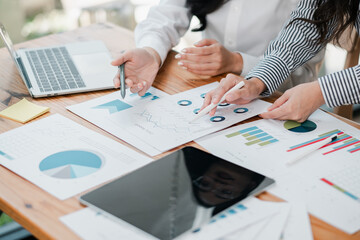 Business professionals reviewing financial charts and graphs on a wooden table, using a laptop and tablet for analysis.