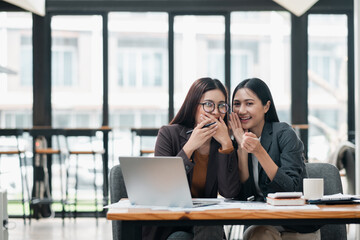 Fototapeta premium Two professional women laughing together in a contemporary office environment, showcasing teamwork and collaboration.