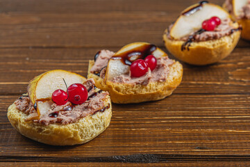 three toasts with chicken liver pate with pear and cranberry on a wooden table