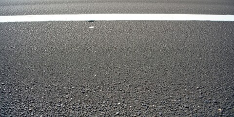 Fototapeta premium A close-up perspective of a black asphalt road surface, featuring a single white line painted across it, highlighting the rough texture of the asphalt.