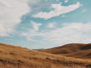 landscape of rolling golden hills under a bright blue sky, with wispy clouds softly scattered across. The scene should convey a sense of tranquility and vastness