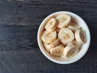 Slices of fresh banana in a bowl on wooden table 