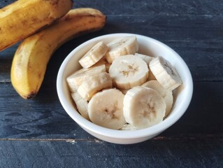 Slices of fresh banana in a bowl on wooden table 