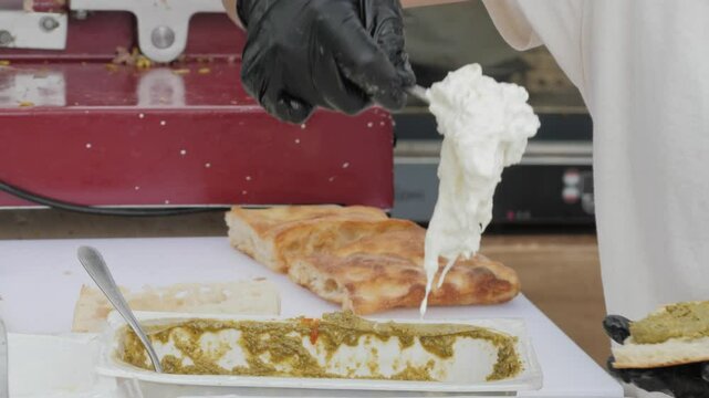 Cooking trendy Italian panini sandwich with focaccia or ciabatta. Slicing salami, mortadella, and ham.Pesto, pistachio sauces and stracciatella cheese. Street food gastronomic festival.