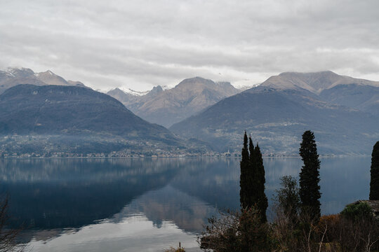 Alpine mountain range reflecting in lake Como on a cloudy winter day