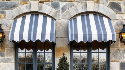 Canopy window awnings in gray and white stripes adding elegance to a stone wall exterior with decorative lighting and greenery below.