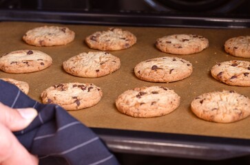 Woman taking baking tray with cookies out of the oven.