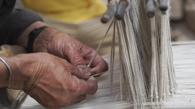 An elderly man meticulously weaves a delicate fabric using a old antique traditional wooden loom, demonstrating skill and patience in Ladakh, india