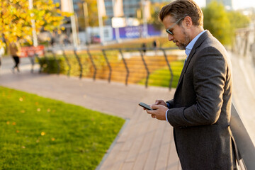 A stylish man enjoys a sunny afternoon while talking on his phone in a vibrant urban setting adorned with fall colors