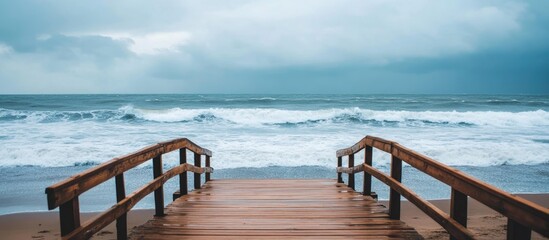 Scenic wooden bridge extending into tranquil sea views under overcast skies with waves gently crashing on the shore