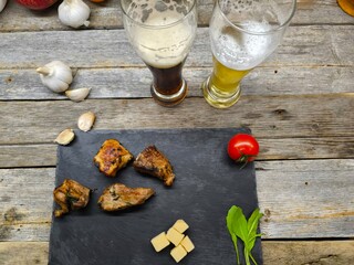 Delicious pieces of shish kebab lie on a sliced board next to glasses of dark and light beer.