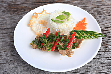 Pad kra pao moo (stir-fried thai basil with pork) and fried egg on old wood scene 