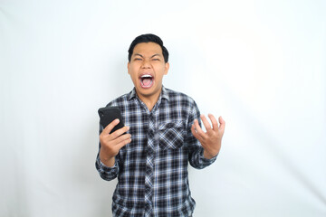 Naklejka premium furious asian man screaming holding smartphone with angry face wearing casual shirt isolated on white background